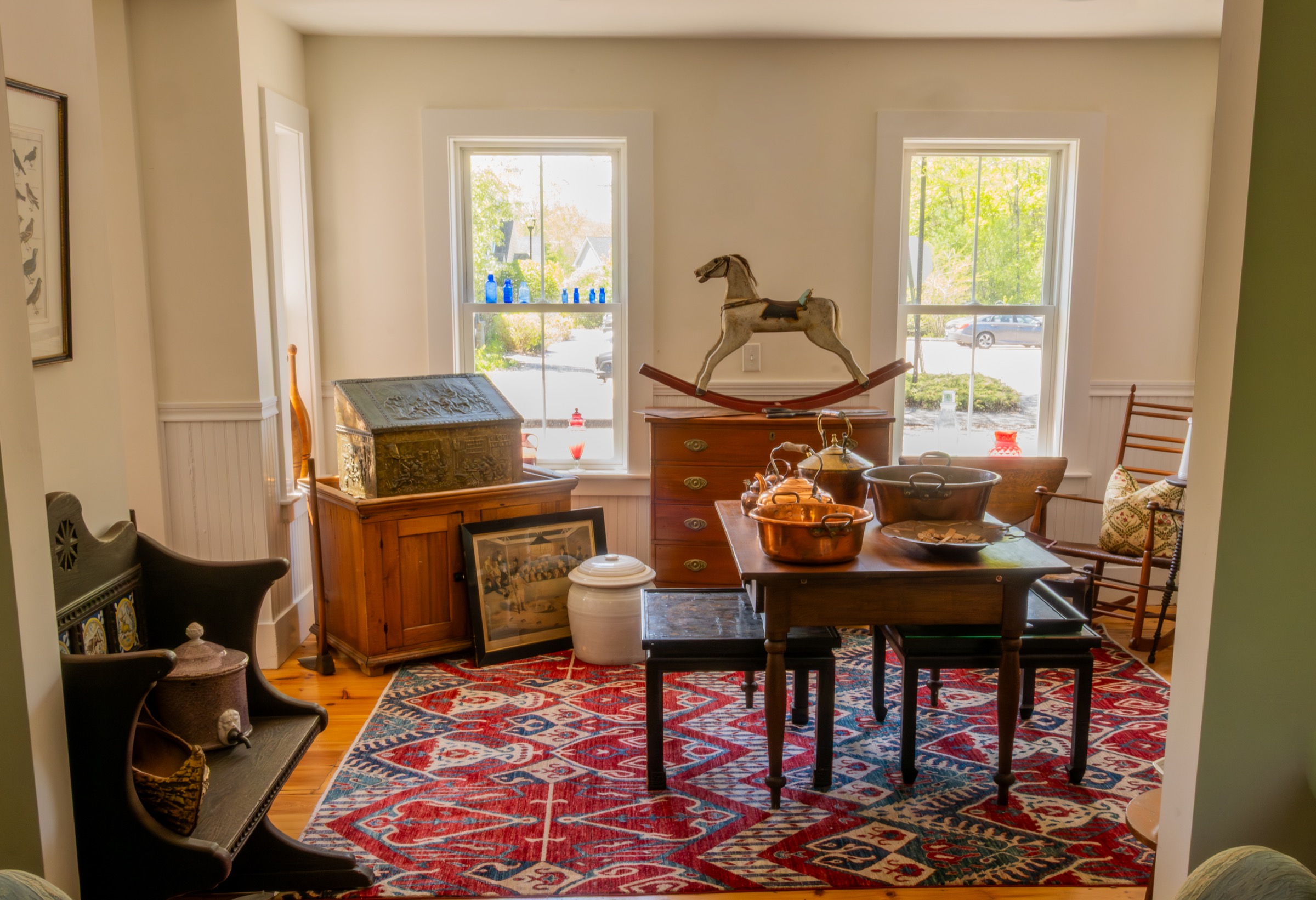 Room display with antique furniture, copper pots, rugs, and a rocking horse.