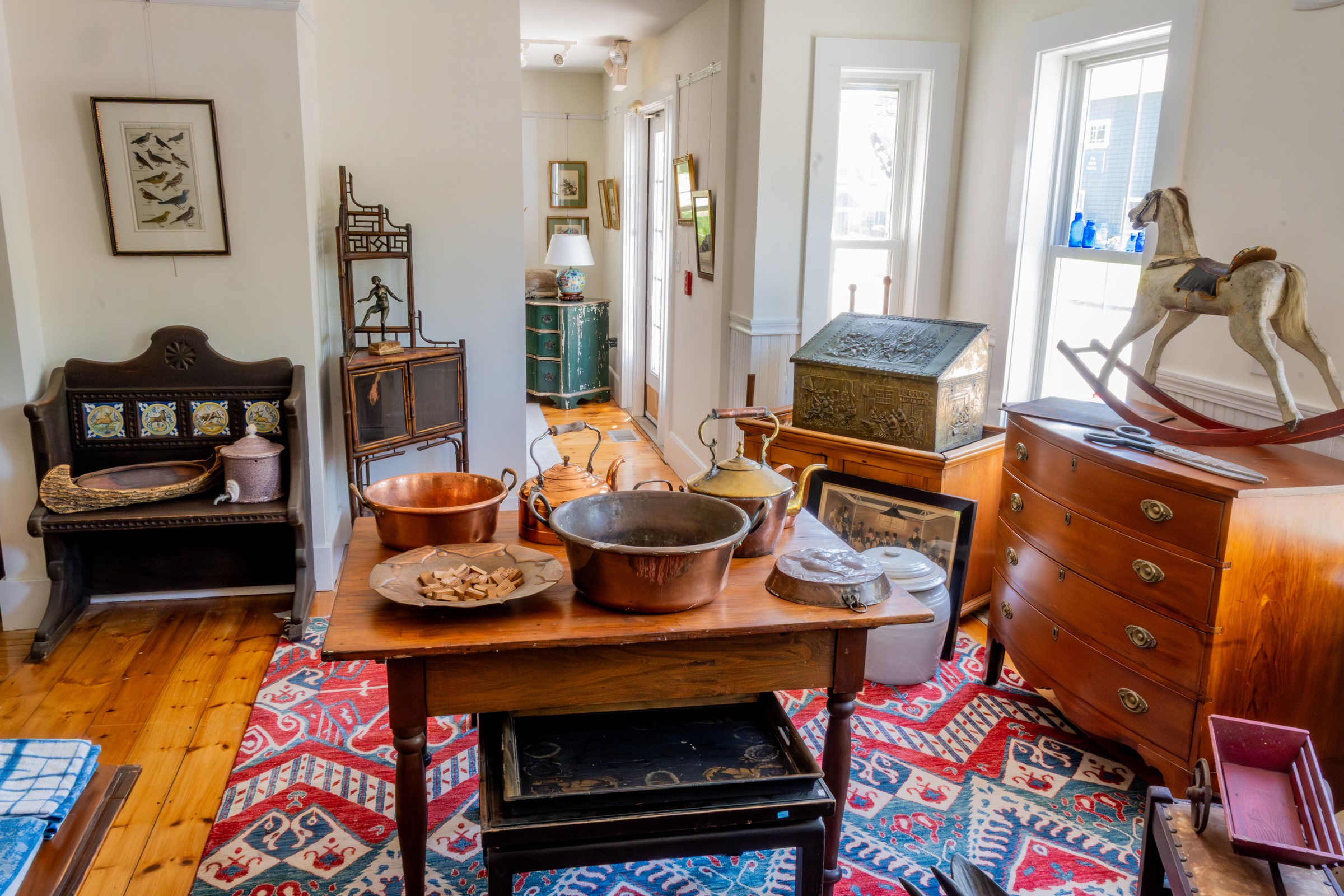 Display room with antique furniture, rugs, copper pots, and a rocking horse.